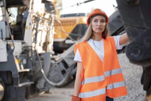 Young woman in protective gear standing by heavy machinery, representing attracting younger workers to mining