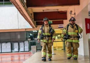 Two firefighters in safety gear walk through a hallway, inspecting access systems for mining safety. 