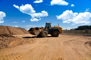 Excavator operating on sandy terrain during ground support scaling, highlighting equipment use in mine safety and slope stabilization.